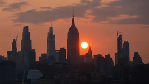 Getty Images The sun is shrouded by smoke from wildfires in Canada as it rises behind the skyline of midtown Manhattan, the Chrysler Building and Empire State Building in New York City on June 11, 2025, as seen from Jersey City, New Jersey