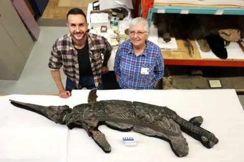 Dean Lomax Two ichthyosaur experts stand behind a two metre long skeleton of an ichthyosaur.