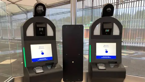 Two of Eurotunnel's EES kiosks. Each machine has a camera and a touchscreen which reads "Welcome/ Bienvenue". 