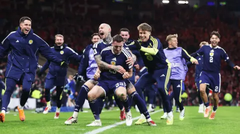 SNS Scotland players wearing dark blue shirts celebrating with Kenny McLean during Scotland's win over Denmark.